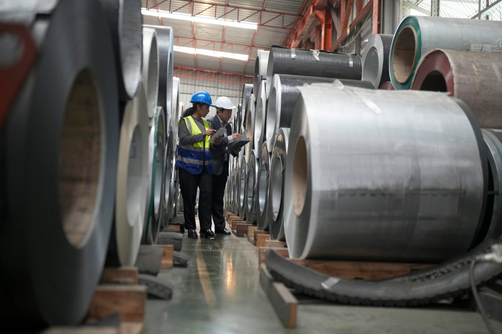 Team members in hard hats reviewing aluminum coils in a warehouse aisle