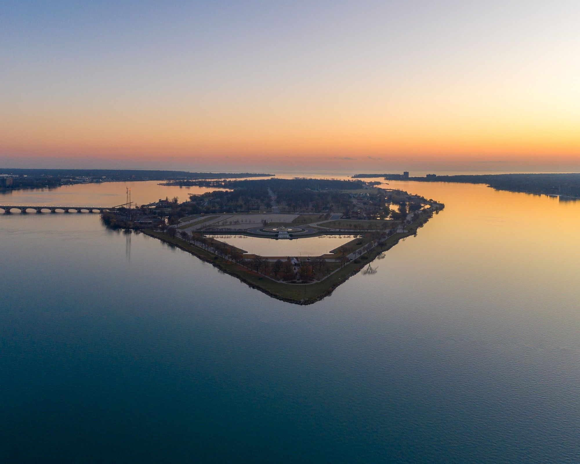 Aerial view at sunset of an island in a wide river, with a bridge and shorelines on either side