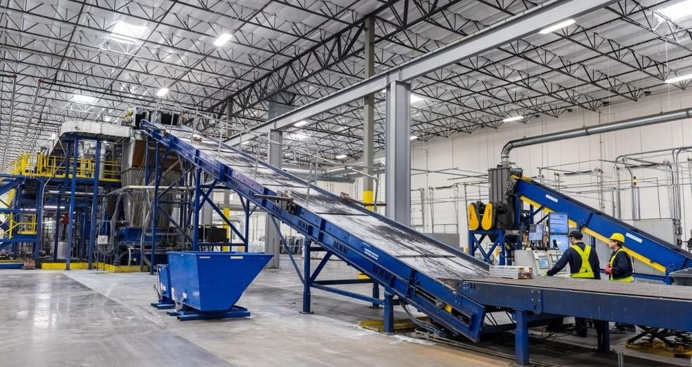 Bright recycling facility with blue conveyor lines and two operators in hard hats at a control station