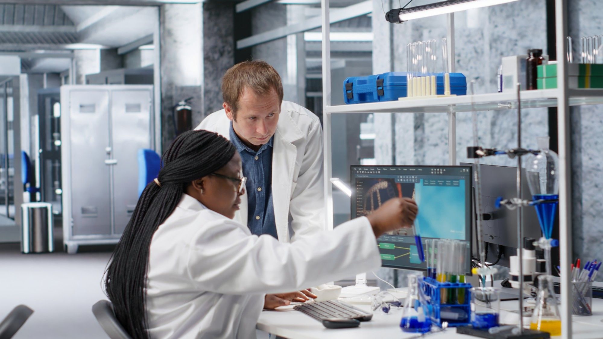 Two scientists in lab coats reviewing results on a screen in a materials lab