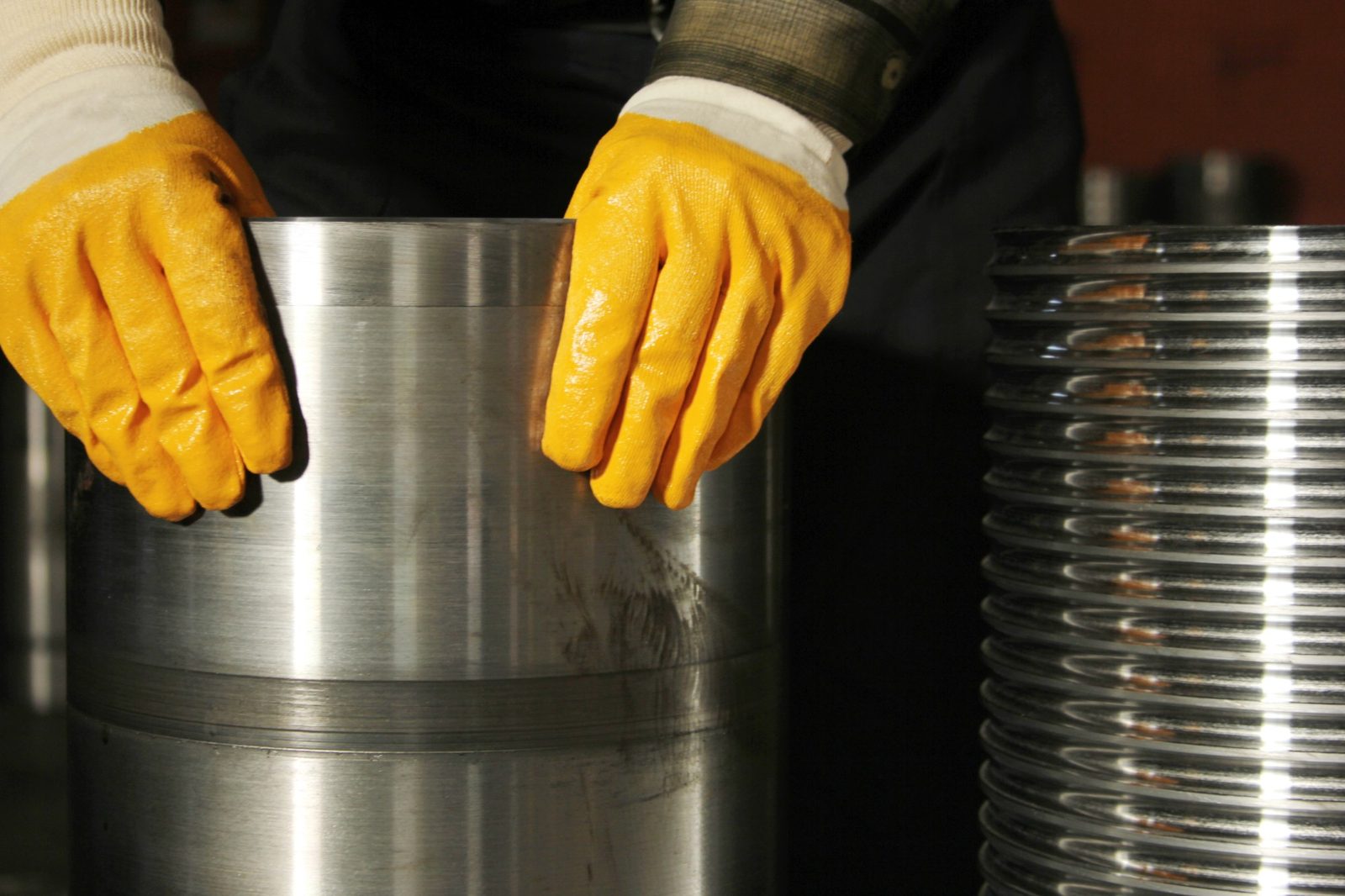 Gloved hands handling a machined metal cylinder beside a polished threaded part