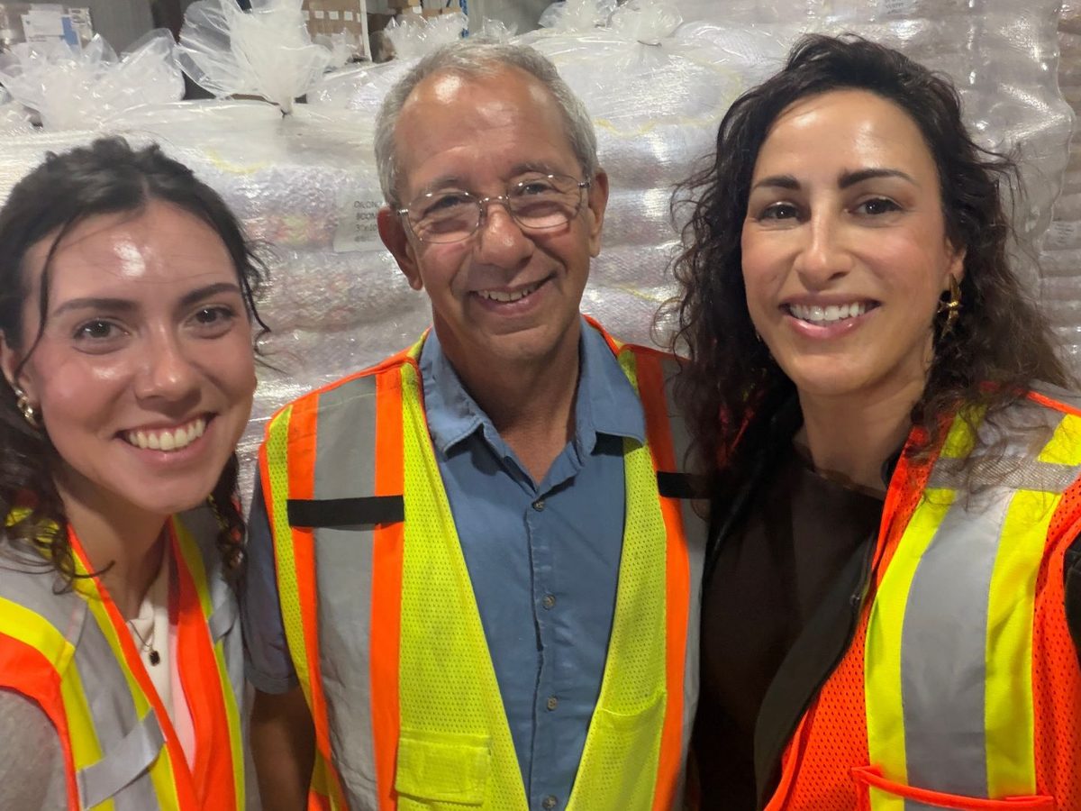 Three CLN team members in high-visibility safety vests on a warehouse floor, with wrapped pallets of product behind them
